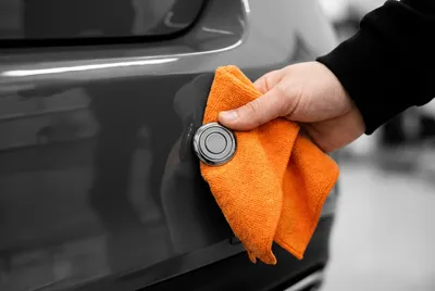 Main nettoyant délicatement le capteur radar d'un pare-chocs avec un chiffon en microfibre.